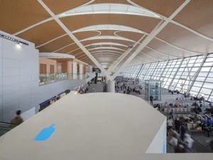 A spacious and modern airport terminal with a high, curved wooden ceiling adorned with circular lighting fixtures and expansi