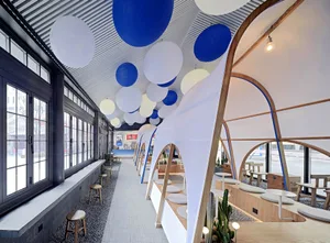 Modern cafe interior with fabric ceiling, wooden benches, white walls, and hanging blue balloons.