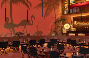 A modern restaurant bar with metal tables, wooden chairs, and glass decor.