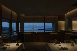 A spacious, well-lit interior of a modern restaurant that features a prominent view of the sea and mountains through large wi