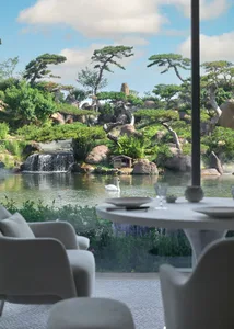 A serene restaurant with a glass window overlooking a waterfall and lush greenery.