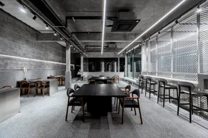 A modern restaurant interior featuring concrete and metal materials, with tables, chairs, and minimalistic design elements.