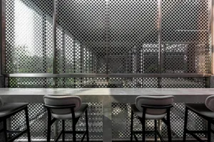 Modern restaurant bar featuring a concrete countertop, stools, and a perforated metal back wall.