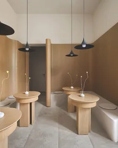 A minimalist restaurant interior with wooden tables and black pendant lights hanging from the ceiling.