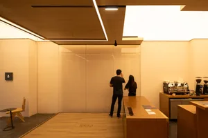 Two people writing on a whiteboard in a modern wooden coffee shop interior.