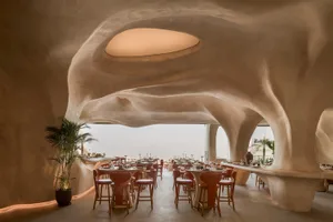 A modern restaurant with concrete walls and ceiling, featuring round tables and high chairs.
