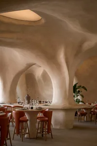 A contemporary restaurant interior with textured, concrete columns and minimalist furniture.