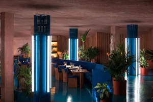 Interior view of a modern restaurant featuring blue light columns, concrete walls, and indoor plants.