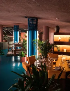 A modern restaurant interior with metallic columns, indoor greenery, and round tables.