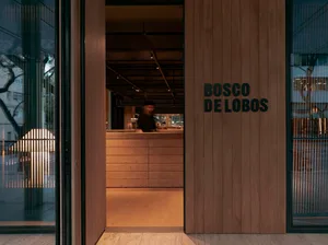 A wooden paneling door with a glass window and the text "BOSCO DE LOBOS" on it, leading into a coffee shop interior.