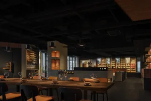 Modern, industrial restaurant interior with concrete walls and wood accents, featuring a long communal table and a monochroma