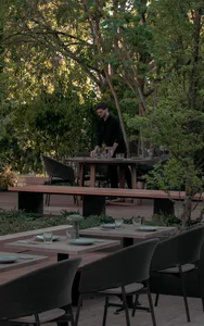 A modern restaurant terrace with wooden furniture and greenery surrounding the dining area.