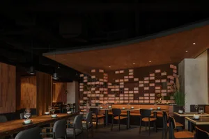 A stylish restaurant interior with brick walls and concrete accents, featuring modern furnishings and dim lighting.
