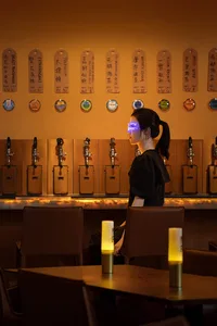 A person sitting in a dimly lit restaurant bar with wooden tables and chairs, leather seating, metal beer taps, and illuminat