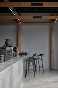 A minimalist industrial-style coffee shop bar with concrete countertops, wooden beams, and metal furniture.