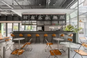 A modern cafe with a metal bar counter featuring sleek glass tables and vibrant yellow seats.
