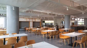 Modern cafeteria interior with minimalist design, concrete and wooden elements, and ample seating.