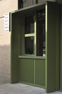 Green metal and glass storefront with glass window and brick wall in the background