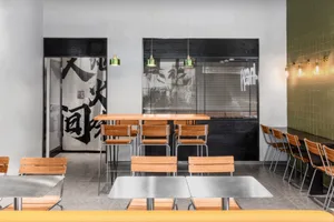 Modern minimalist restaurant interior with wooden tables, metal chairs, concrete flooring, and industrial lighting.