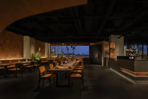 A modern restaurant interior featuring wooden tables, concrete walls, and plant life