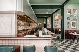 A restaurant interior featuring a tile-walled bar with brass accents and concrete countertops.