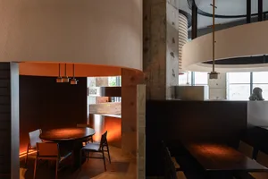 Modern industrial restaurant interior with wooden tables and chairs, concrete walls, and circular pendant lights.