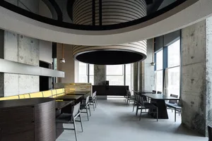 Modern restaurant interior with concrete walls, wooden furniture, and large windows.