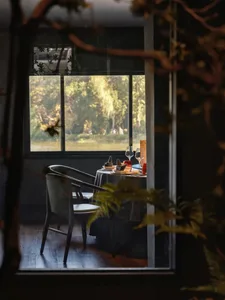 A modern restaurant with wooden chairs, glass table, and upholstered fabric seating.