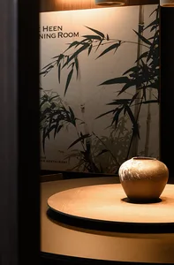 A circular wooden table with a ceramic vase in the center, featuring a bamboo plant poster in the background.