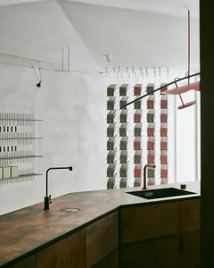 A modern kitchen with a metallic countertop, industrial style lighting, and a row of suspended shelves.