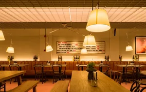A modern industrial restaurant interior with wooden tables, leather booths, and metallic chairs.