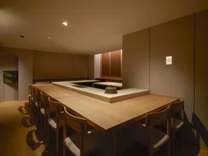 A modern restaurant interior featuring wooden tables and chairs under warm lighting.