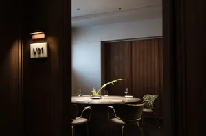 A modern, private dining room with wooden walls, a round table, and green chairs.