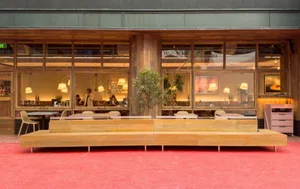 A modern restaurant interior with wooden seating, glass wall, and carpet floors.
