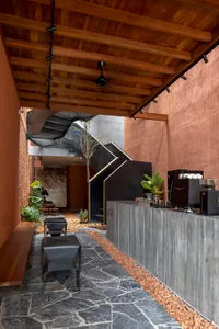 A modern coffee shop with concrete floors and glass walls, featuring a bar counter and a seating area with stools.