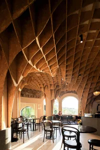 Interior of a modern restaurant with a high, wooden, geometric ceiling and multiple dining tables and chairs.