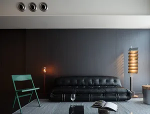 Modern living room with a black sofa, dark wood paneling, and a green folding chair.