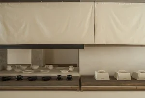 A modern coffee shop display featuring wooden shelves with white ceramic dishes and black coffee cups.