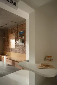 Interior design of a modern coffee shop extension featuring exposed concrete, brick walls, and wooden seating.