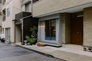 A modern storefront with a concrete exterior, featuring large windows, a wooden bench, and potted plants.