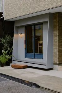 A modern storefront with a large window, wooden bench, and potted plants on the sidewalk.