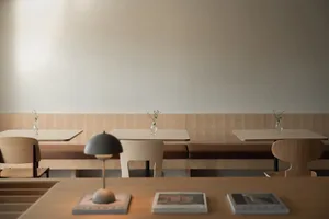 A modern restaurant with minimalist design, wooden seating, and small flower arrangements.