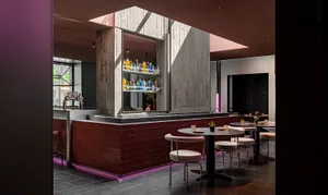 Modern cafe-bar interior with concrete walls and tables surrounded by chairs.