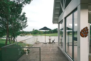Wooden deck with glass railing overlooking a serene water body. Modern furniture and decorative elements.