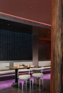 Modern restaurant interior with black tiles, metallic furniture, and purple lighting