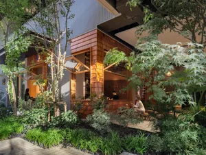 A modern restaurant exterior made of wood with greenery surrounding it.