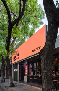 A modern restaurant storefront with an orange facade, surrounded by green trees and featuring a sleek, contemporary design.