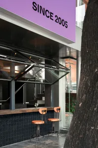 A modern street view cafe bar with glass panels, concrete walls, and wooden seating.