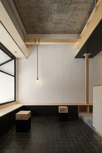 A minimalist living space featuring a concrete wall, black tiled floor, and wooden furniture.