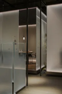 Modern restaurant private dining room with glass walls, wooden floor, and decorative plants.